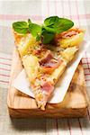 Slice of Hawaiian pizza with fresh oregano on chopping board