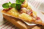 Slice of Hawaiian pizza with fresh oregano on chopping board