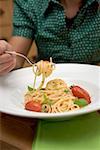 Woman behind plate of spaghetti with tomatoes and basil