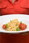 Woman holding plate of spaghetti with tomatoes and basil