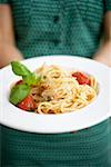 Femme tenant assiette de spaghettis au Parmesan et basilic