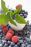 Blueberries and raspberries with leaves, some in bowl