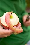 Child's hands holding a half- peeled red apple