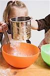 Two children baking (sieving flour into bowl)