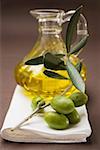 Olive sprig with green olives, carafe of olive oil behind