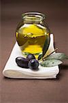 Olive sprig with black olives, jar of olive oil behind