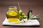 Green olives on twig beside jar of olive oil