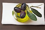 Olives noires sur une brindille sur le verre d'huile d'olive