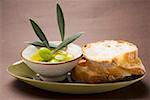 Olive sprig with green olives in bowl of olive oil, white bread