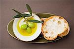 Green olives on twig in bowl of olive oil, white bread