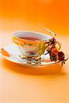 Rose hip tea in china cup, fresh rose hips in saucer