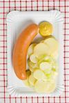 Frankfurter with potato salad and mustard on paper plate