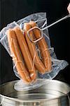 Putting frankfurters in bag into pan