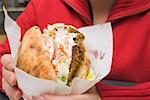 Person holding pita bread filled with falafel in snack bar