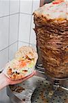 Hand holding a döner kebab (opened), meat on spit