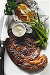 Grilled beef steak with baked potato, beans and dip