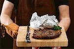 Man holding grilled beef steak on chopping board