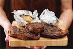 Man holding grilled beef steaks on chopping board