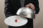 Butler serving cherry tomato on plate with dome cover