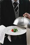 Butler serviert Tomate und Petersilie auf Teller mit Domdeckel