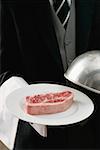 Butler desservant le steak de bœuf cru sur plaque avec dôme translucide