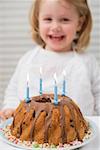 Small girl behind birthday cake with candles