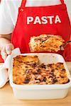Woman taking portion of lasagne out of baking dish