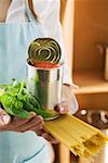 Woman holding spaghetti, tin of tomatoes and basil