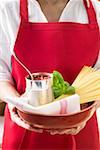 Woman holding tin of tomatoes, spaghetti and basil