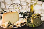 Olives, cheese, crackers & olive oil on table out of doors