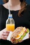 Woman holding sandwich and bottle of orange juice