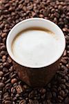 Cup of coffee with milk froth on coffee beans