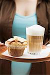 Woman holding tray with latte macchiato and muffin