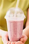 Hands holding blueberry smoothie in plastic beaker