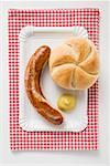 Sausage (bratwurst) with mustard & bread roll on paper plate