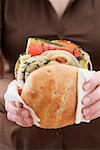 Woman holding toasted roll filled with grilled vegetables