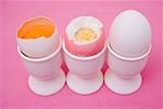 Three eggs in eggcups (raw & boiled with top cut off, whole)