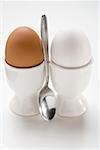 Brown and white eggs in eggcups, spoon between them