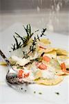 Sprinkling Parmesan onto ravioli with diced tomatoes