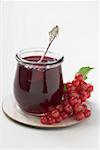 Jar of redcurrant jelly with spoon, redcurrants beside it