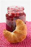 Pot de confiture de framboise, croissant au premier plan