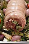 Raw rolled pork joint with vegetables on baking tray