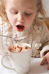 Small girl spooning cocoa with marshmallows out of cup