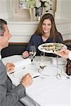 Waiter serving fresh oysters to man & woman in restaurant