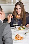 Man offering woman prawn on fork in restaurant