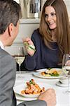 Woman offering man asparagus on fork in restaurant