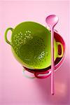 Coloured colanders, stacked, and pink cooking spoon