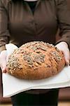 Woman holding wholemeal bread with pumpkin seeds on linen cloth