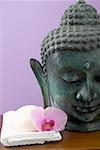 Orchid and soap on white towel beside statue of Buddha