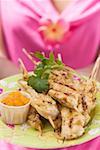 Woman holding plate of satay and chutney